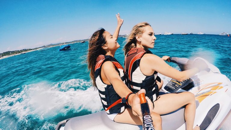 Two women on a jet-ski taking a photo of themselves using a selfie stick.