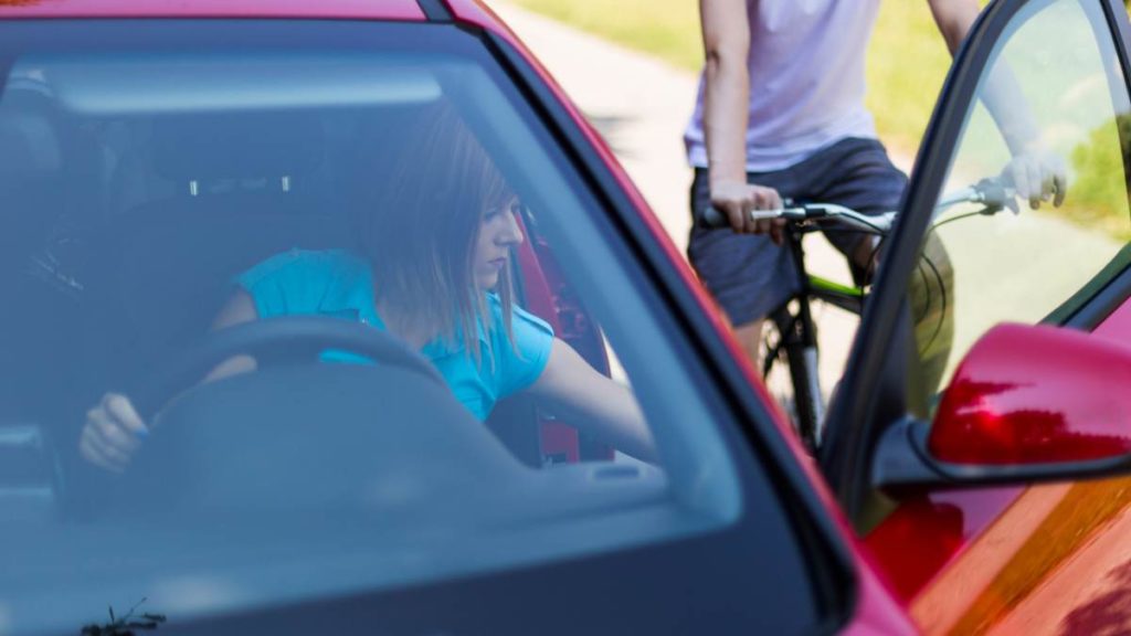 Woman in a car opening her door while a cyclist approaches.