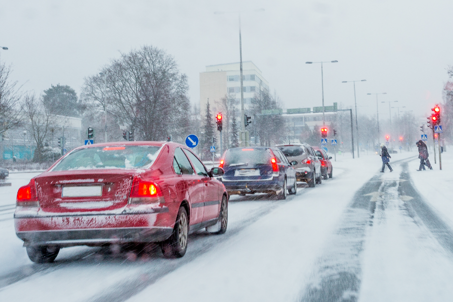 Cars lined up on a snowy road, waiting for pedestrians to cross.