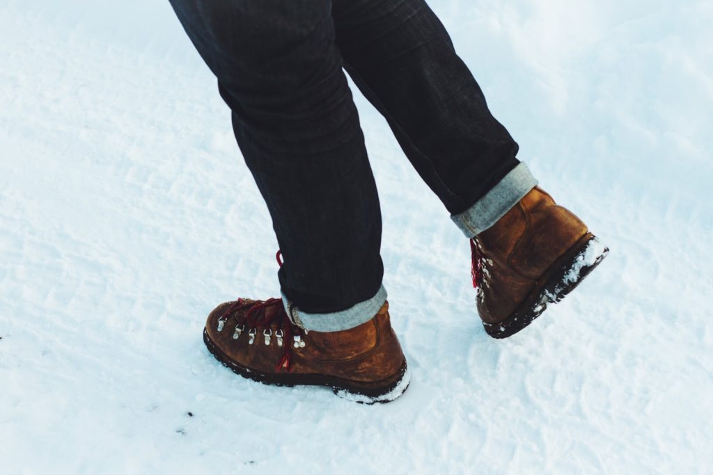 Legs seen from the knee down wearing jeans and brown boots, on a snowy ground.