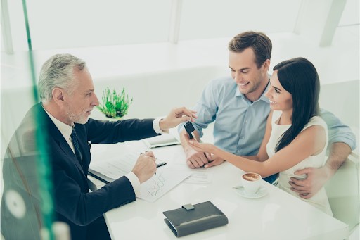 Real estate agent handing keys to a couple while filling out a contract.