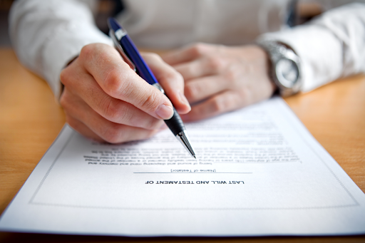 Hands holding a pen over a document titled "Last Will and Testament of".